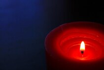 A picture of a lit red candle with a dark blue background.