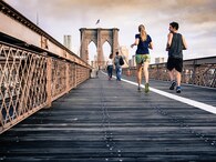 A picture of a couple running together on a bridge.