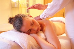 A picture of a woman lying on a massage table being gently touched on her back by a massage therapist.
